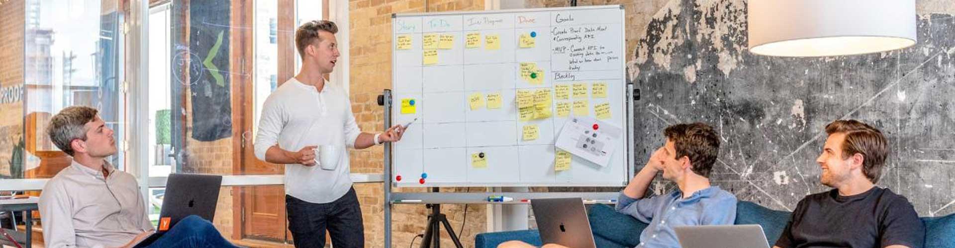 A Group of People Sat Around a White Board with Computers